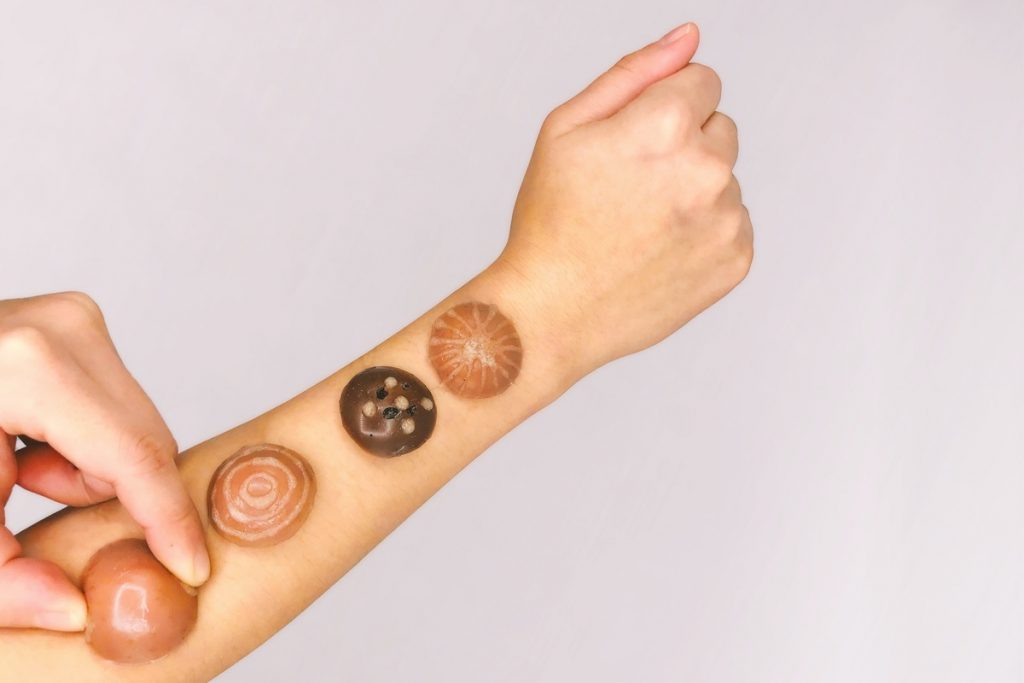Image of the Swatches applied an a human arm: four blobs on an arm and the other hand manipulating one of the blobs